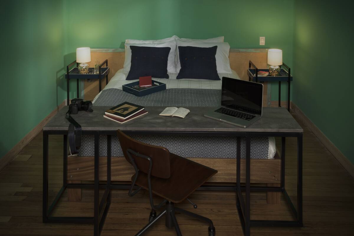 Une chambre bien rangée, avec un lit, des tables de chevet, un ordinateur portable, des livres et une chaise.
