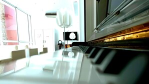 A piano in a room with a large window, a clock, and a modern light fixture. - Grand Hotel Jeanne d'Arc (Lourdes)