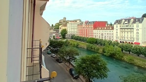 A balcony overlooking a river with buildings in the background. - Grand Hotel Jeanne d'Arc (Lourdes)