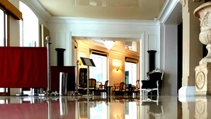 A spacious lobby with a polished floor, a red curtain, and classical columns. - Grand Hotel Jeanne d'Arc (Lourdes)