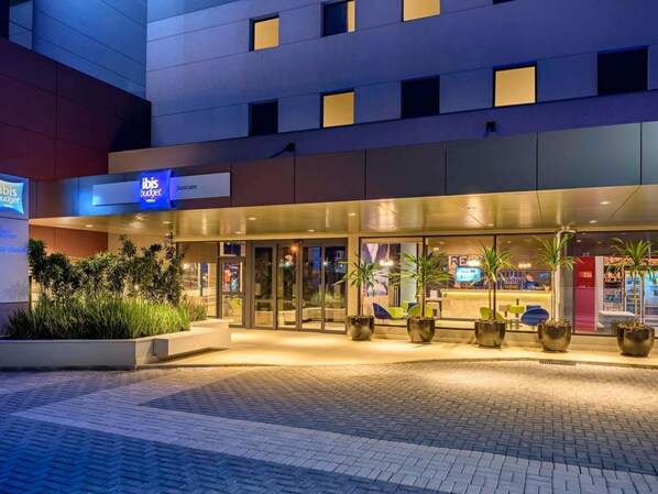 Ein Hotel mit gläserner Fassade, Sitzgelegenheiten im Freien und Blumentöpfen.