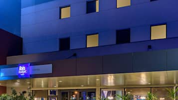 Un moderno edificio de hotel con un llamativo letrero de "ibis budget", múltiples ventanas y un área de entrada bien iluminada.
