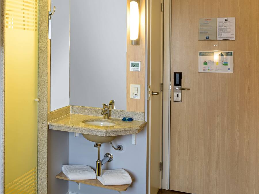 Bany amb rentatge, mirall, para-tovallons i porta de fusta amb una cerradura i un senyal.