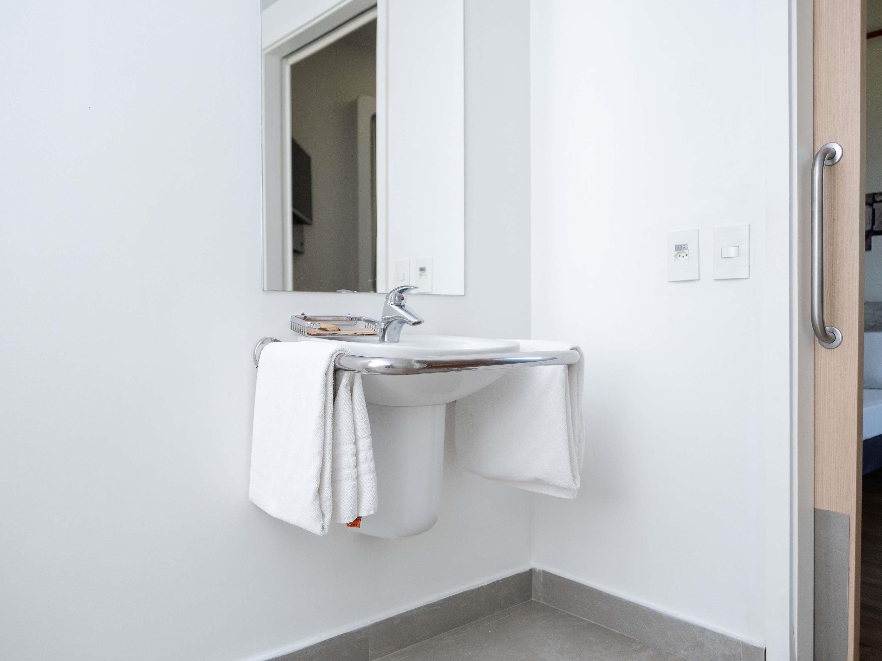 A modern bathroom with a white sink, a mirror, and a towel rack.