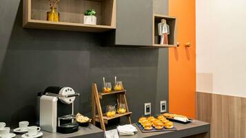 Un bufé de desayuno con máquinas de café, una exposición de frutas y una estación de sándwiches.