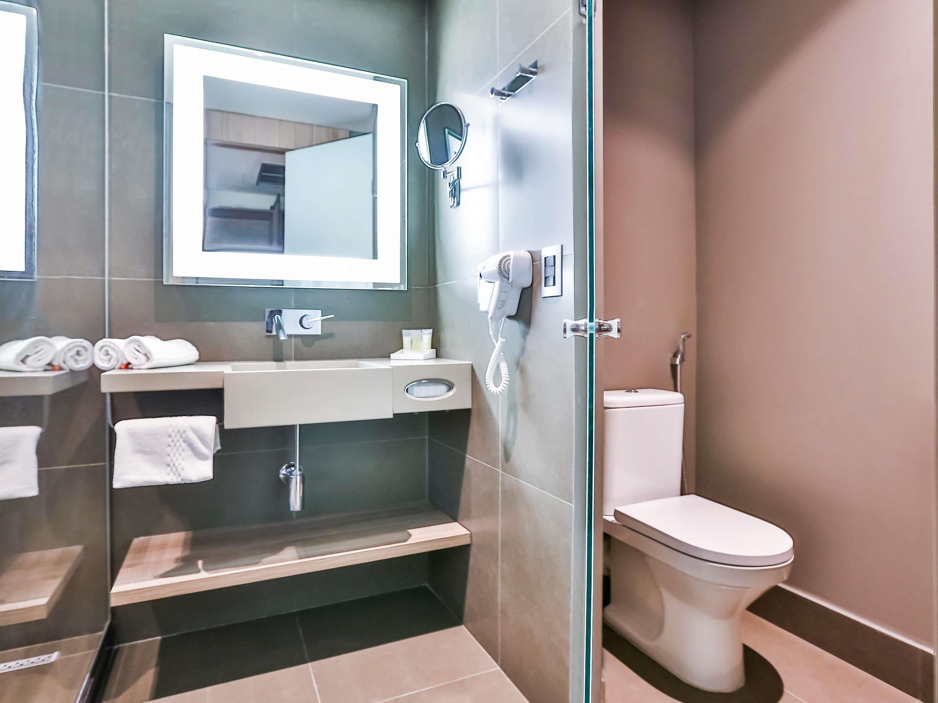 Un baño moderno con cabina de ducha de vidrio, inodoro blanco, lavabo con espejo y toallas ordenadas.