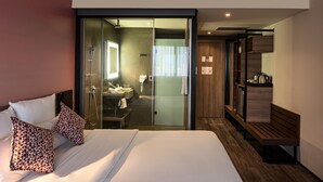 A modern hotel room with a large bed, a glass-enclosed shower, a wooden bench, and a small kitchenette. - Novotel Sorocaba (Sorocaba)