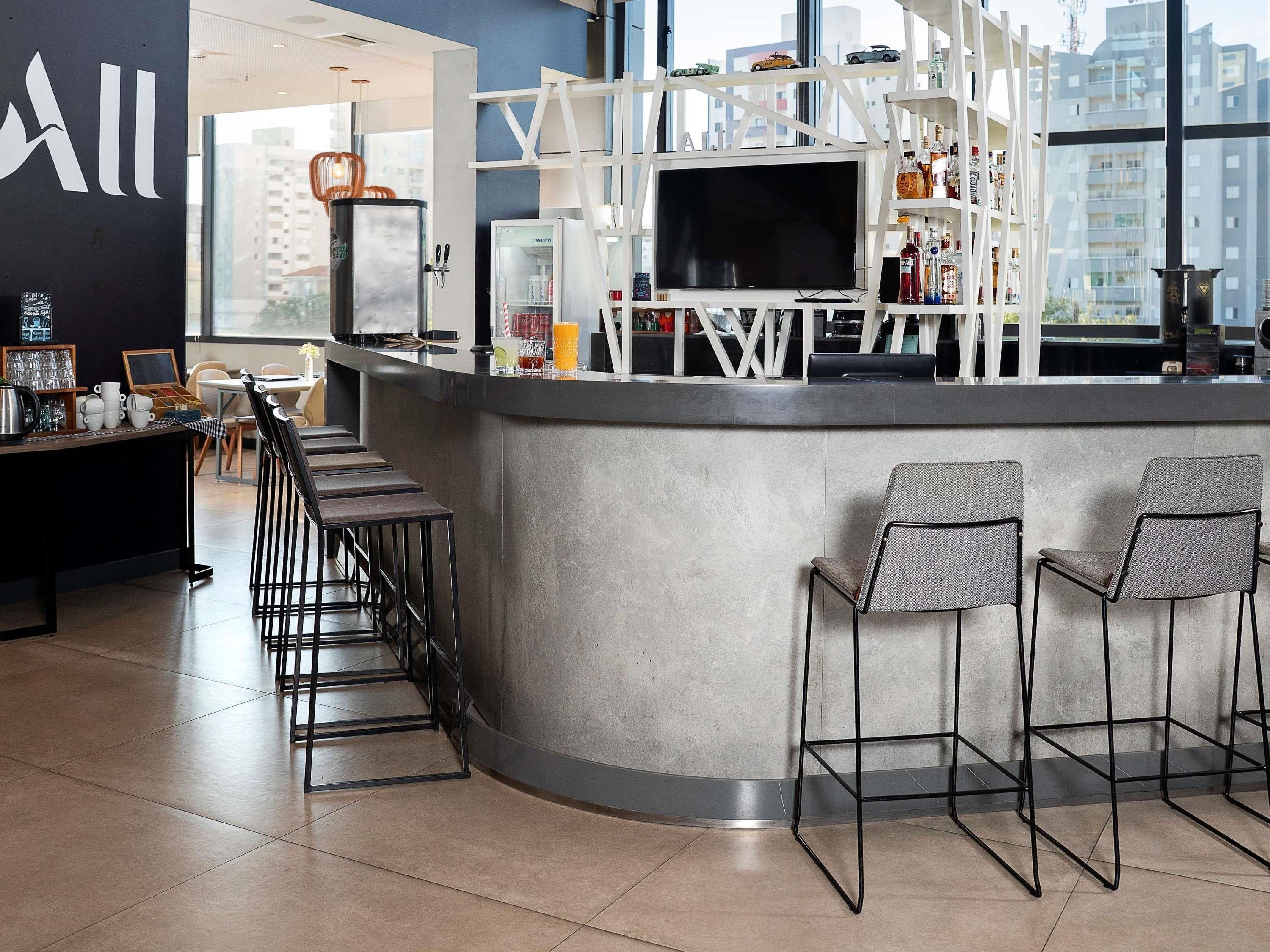Un área de bar moderna con un televisor, estantes con botellas y taburetes.