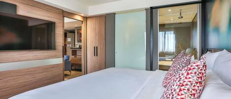 A modern bedroom with a large bed, a TV mounted on the wall, and a sliding door leading to a bathroom.