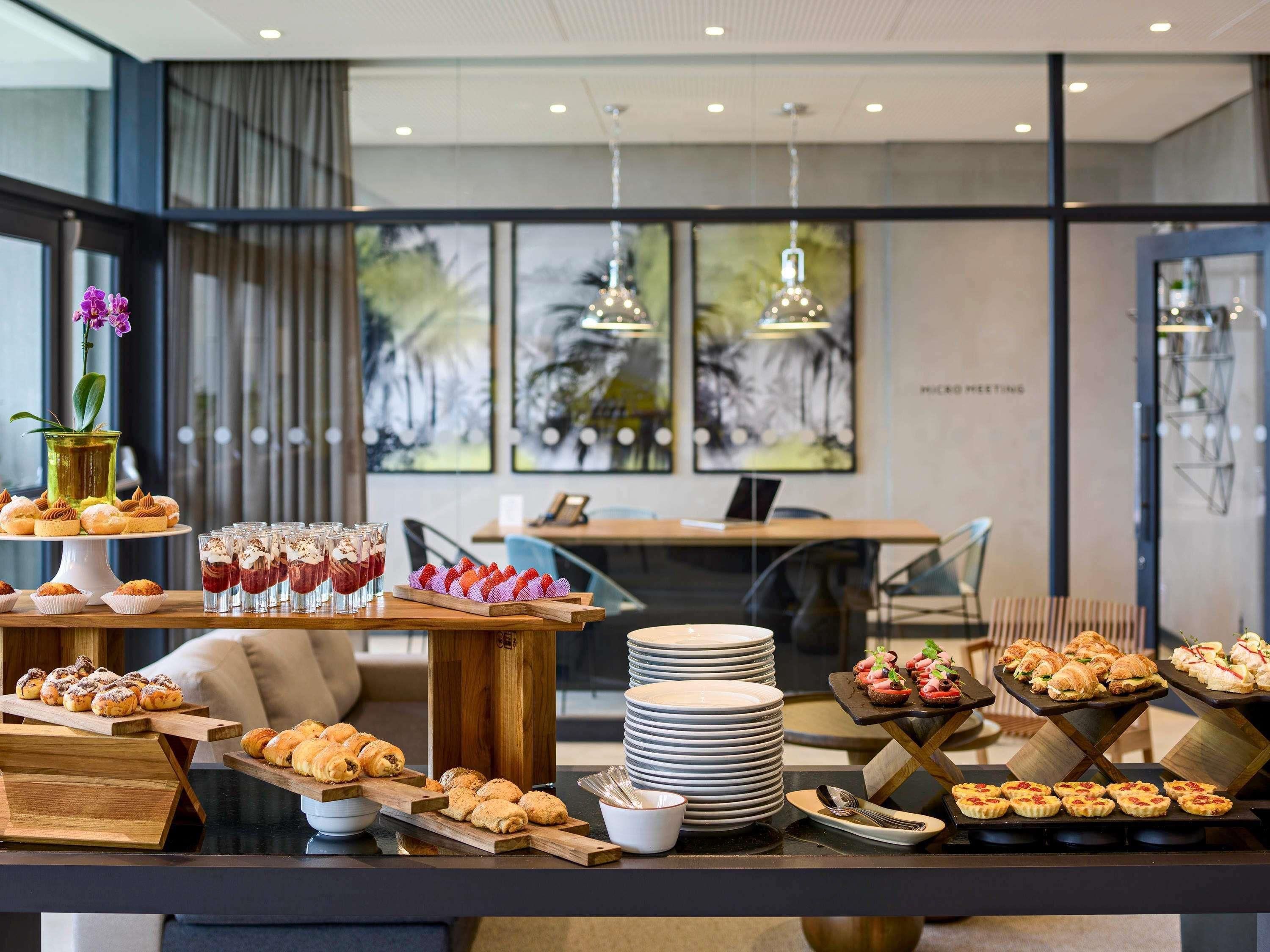 A buffet setup with various pastries and desserts, a coffee station, and a seating area with a view of the outdoors.