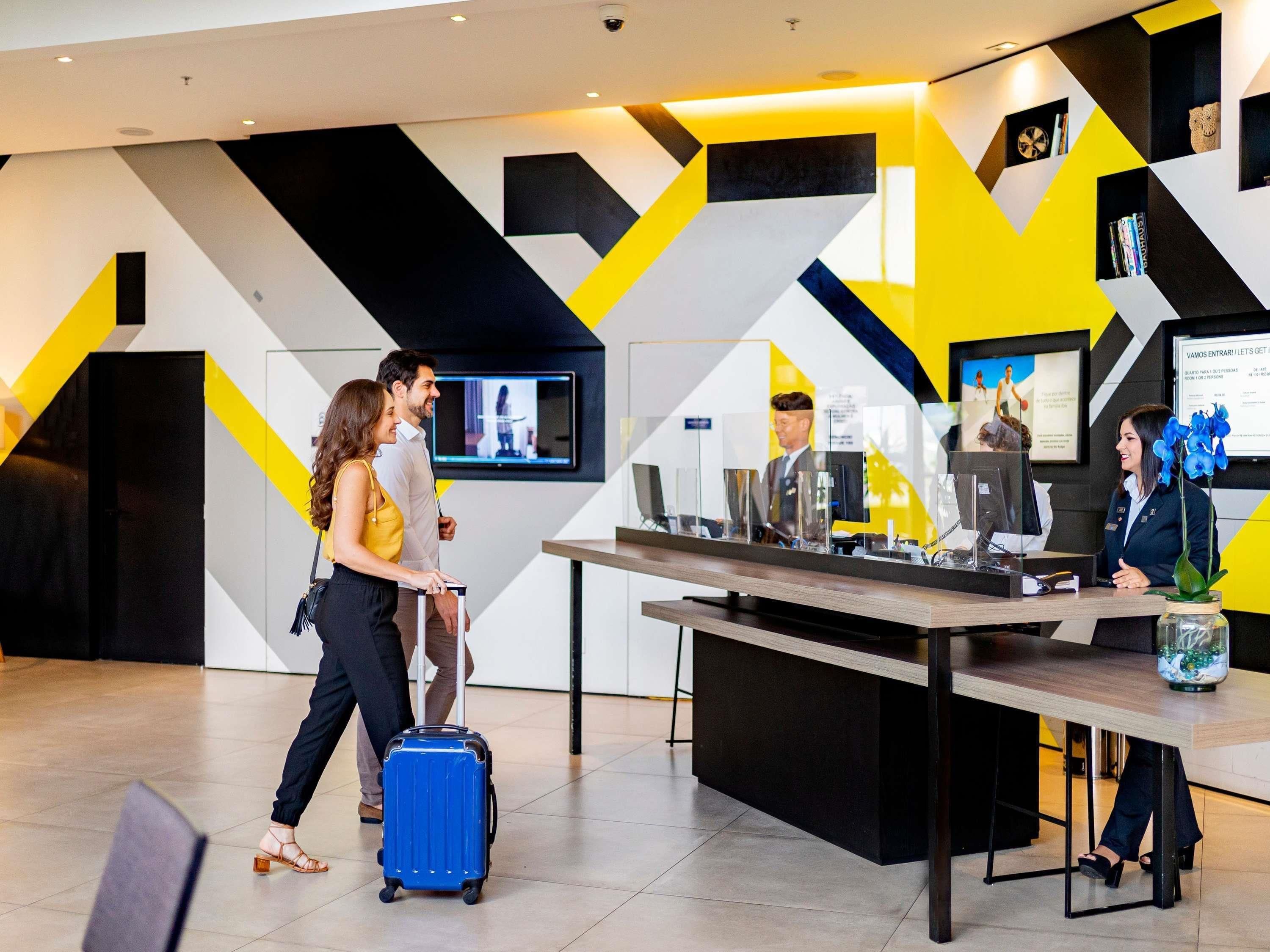 A reception desk with a monitor, a digital screen, and a vase with flowers.