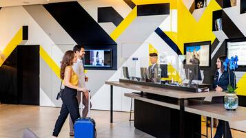 A reception desk with a monitor, a digital screen, and a vase with flowers.