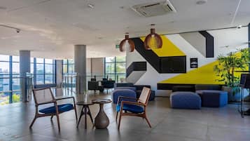 Um hall amplo com mobiliário moderno, janelas grandes e um design geométrico na parede.