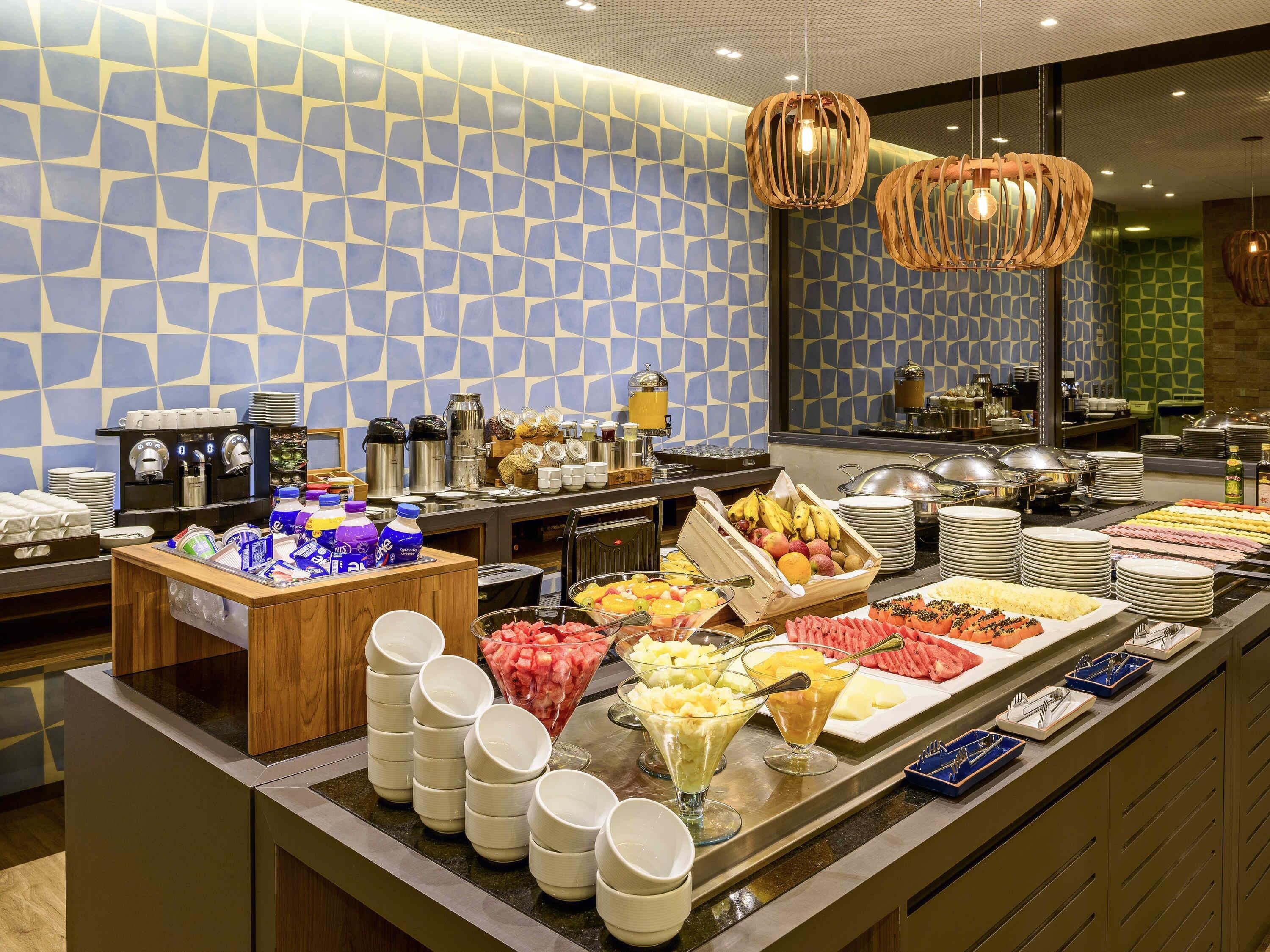 A buffet with various food items and beverages, a coffee station, and a patterned wall.