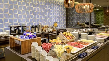 A buffet with various food items and beverages, a coffee station, and a patterned wall.