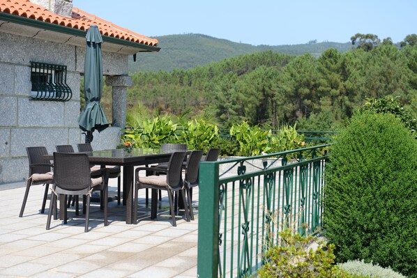 An outdoor patio with a table and chairs, surrounded by greenery and a view of a forested hill. - AboimHouse (Amarante)