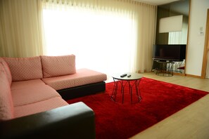 A modern living room with a pink sofa, a red rug, a small round table, and a TV in the background.