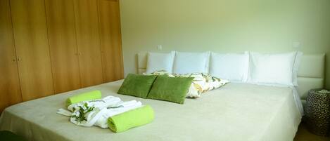 Una cama bien hecha con ropa de cama blanca y verde, un armario de madera y una mesita de noche tejida.