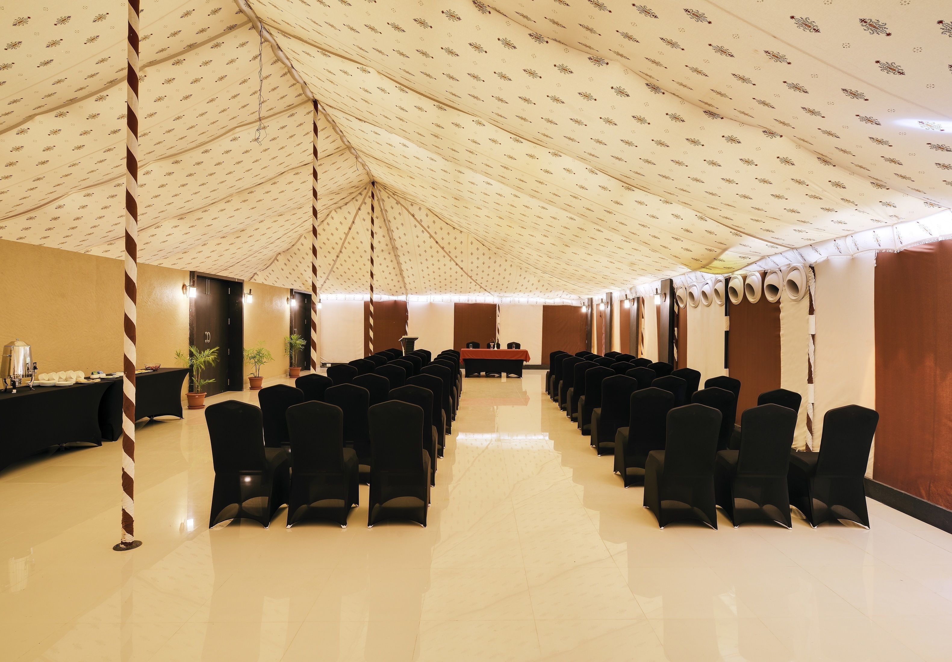 A conference room with rows of black chairs, a long table, and a patterned ceiling.