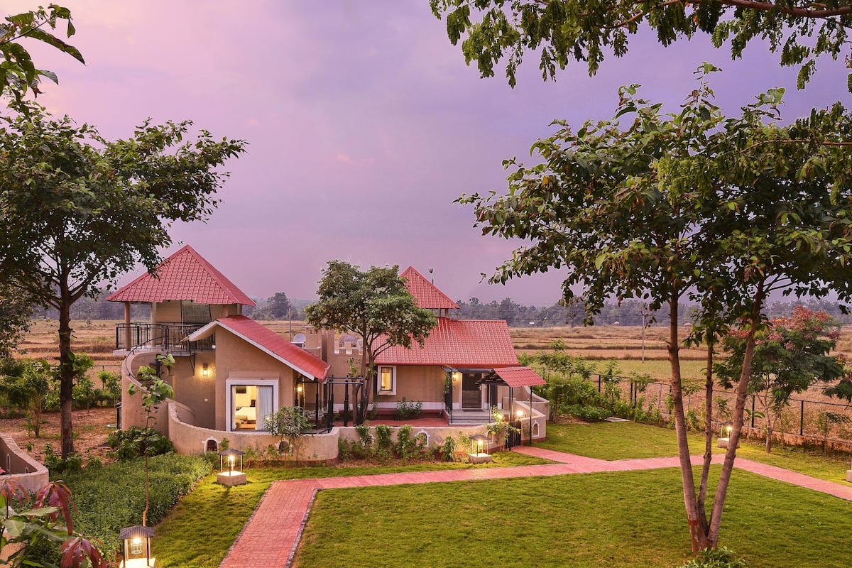 A two-story house with a red roof, surrounded by a well-maintained garden and a view of the countryside.