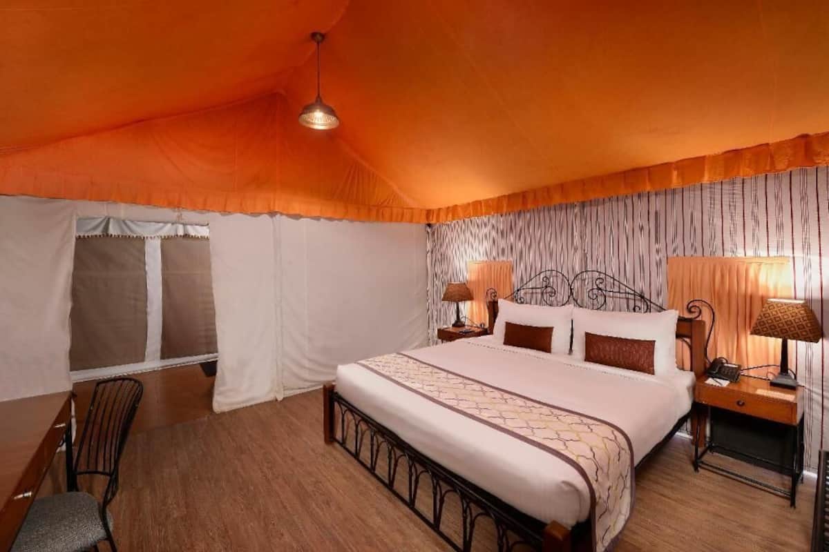 A bedroom with a large bed, two bedside tables, a chair, a window with curtains, and a hanging light fixture.