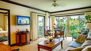 Habitación de hotel con un televisor grande, un área de comedor con sillas y una mesa, un sofá y un balcón con plantas.
