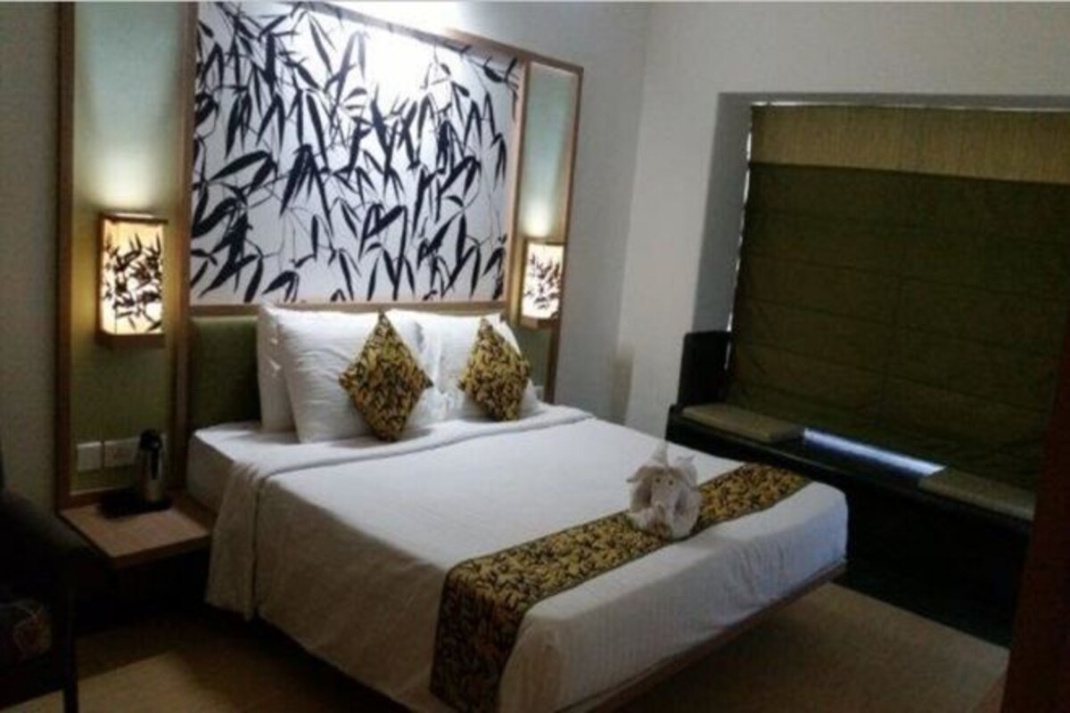 Una habitación de hotel con una cama grande, dos mesitas de noche, una obra de arte en la pared y una ventana con persianas.