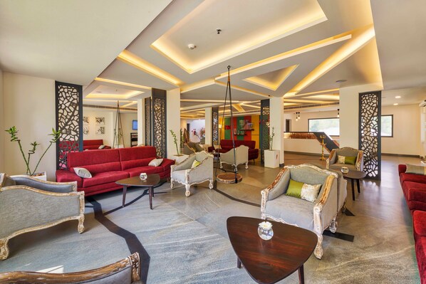 A spacious lobby with a red sofa, grey armchairs, and a wooden coffee table. - Sterling Wayanad (Sulthan Bathery)