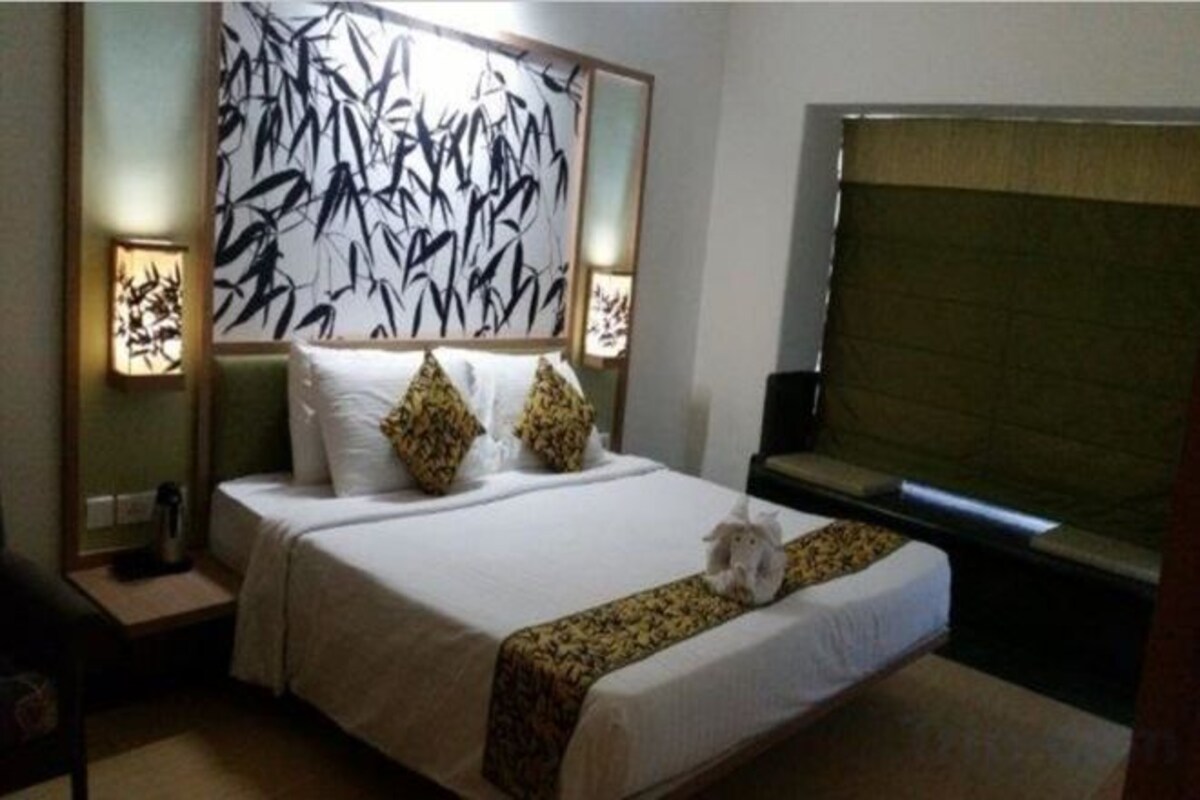 Una habitación de hotel con una cama grande, dos mesitas de noche, un televisor montado en la pared y una ventana con vistas.