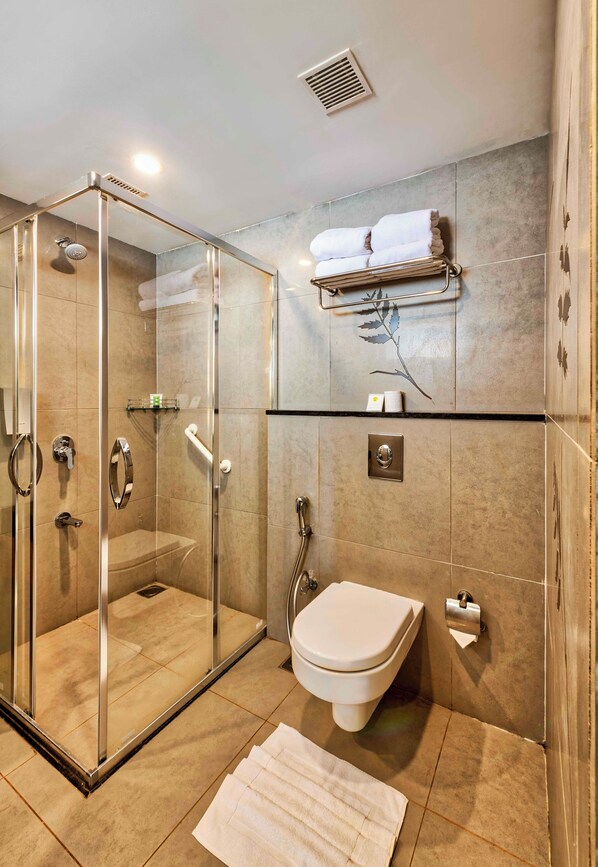 A modern bathroom with a glass-enclosed shower, a toilet, and a towel rack. - Sterling Wayanad (Sulthan Bathery)
