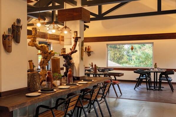 Un restaurante con una barra de madera larga, sillas negras y lámparas colgantes.
