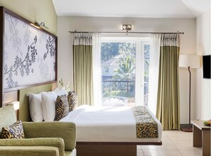 Una habitación de hotel con cama, sofá, un cuadro, una ventana con cortinas y una lámpara.