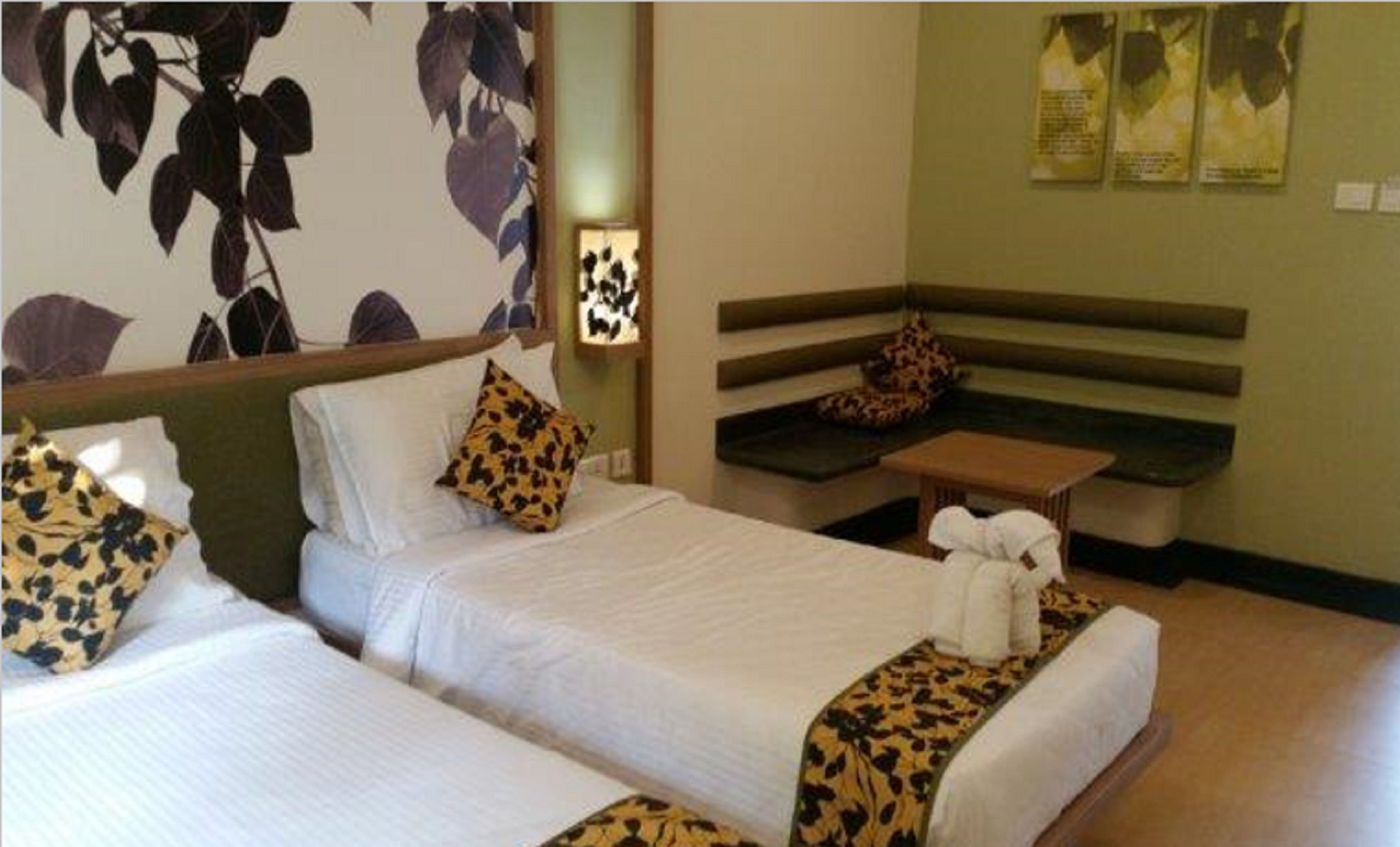 A hotel room with two beds, a bench, and a small table.