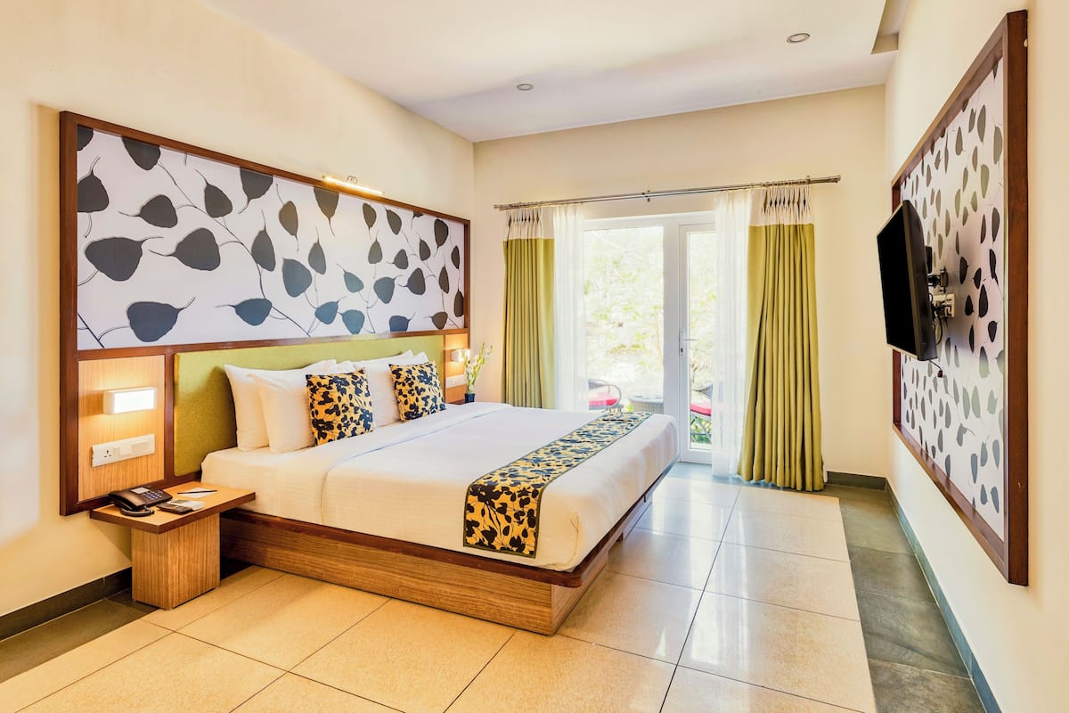 A hotel room with a large bed, a bedside table with a phone, a TV mounted on the wall, and a view of the outdoors through a sliding door.