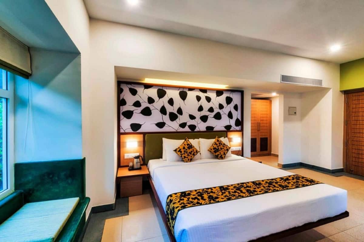 A hotel room with a bed, bedside tables, a headboard with a leaf pattern, and a view of the outside.