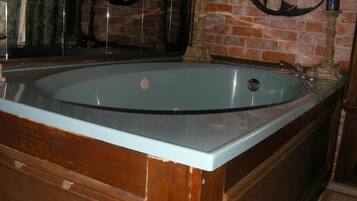 Una bañera grande y rectangular con estructura de madera y frente de cristal, ubicada frente a una pared de ladrillo con detalles decorativos.