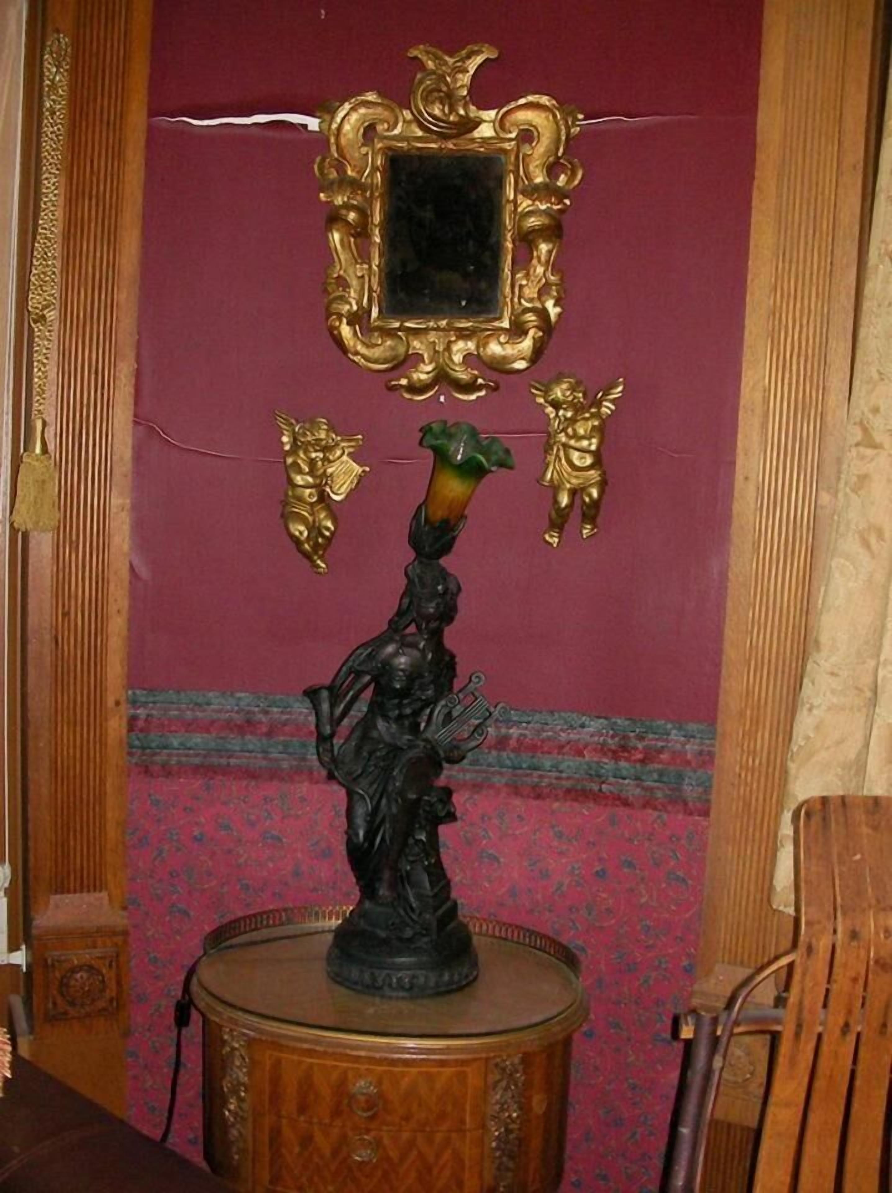 Une statue posée sur un piédestal en bois, avec un miroir au-dessus.