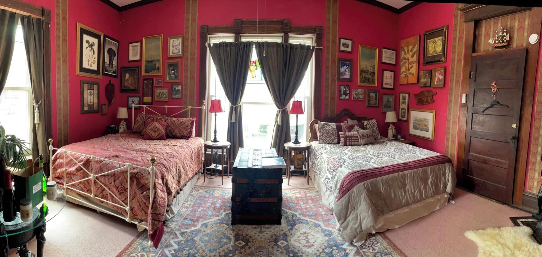 A room with two beds, a chest of drawers, and a large window with curtains.