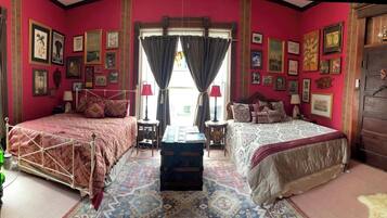 A room with two beds, a chest of drawers, and a large window with curtains.