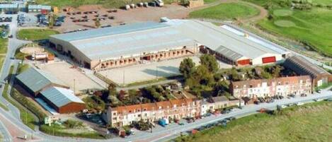 An aerial view of a large industrial building with a flat roof, surrounded by residential buildings and a parking lot.