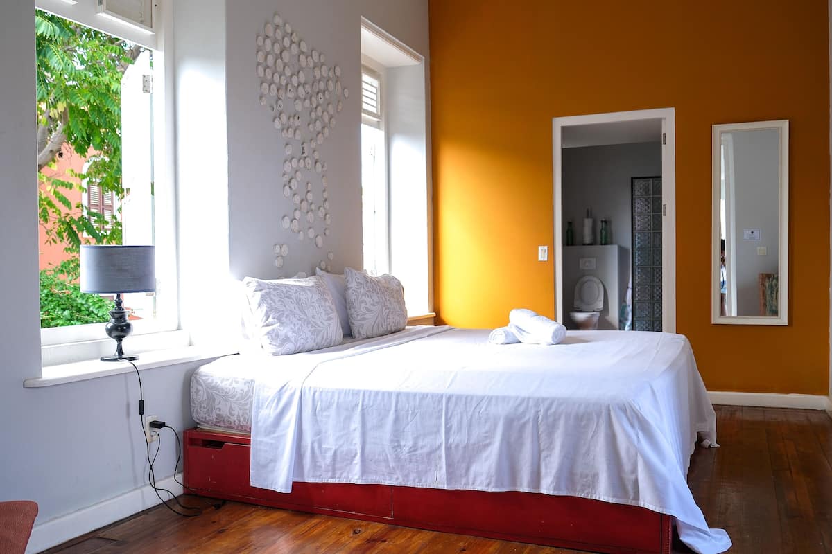 A bedroom with a bed, a window, a red storage unit, and a wall-mounted light fixture.