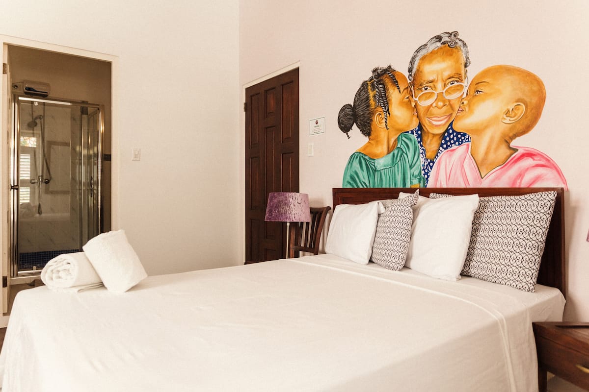 A hotel room with a bed, a shower, a door, and a wall with a mural.