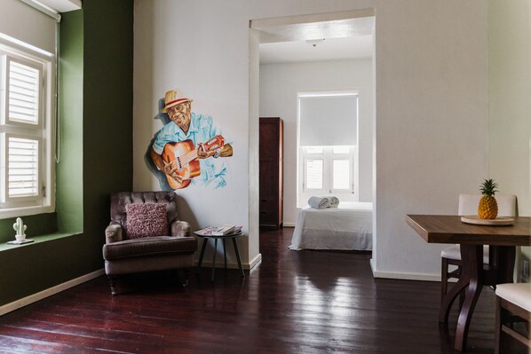 A living room with a mural, a brown leather armchair, a small round table, and a wooden dining table with a pineapple on it. - Bario Hotel (Willemstad)
