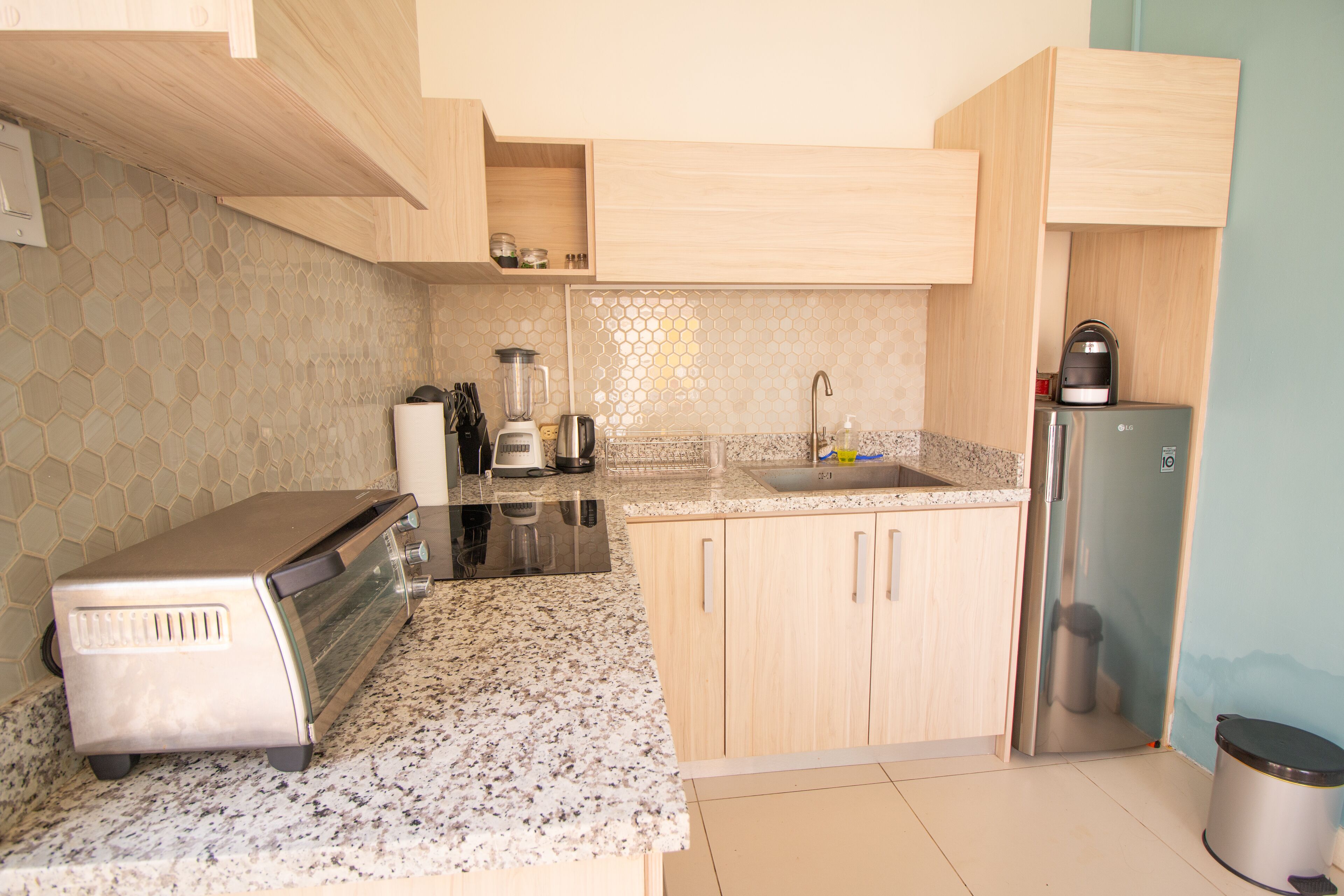 Una cocina con armarios de madera, encimera de granito, tostadora, licuadora, hervidor y refrigerador.