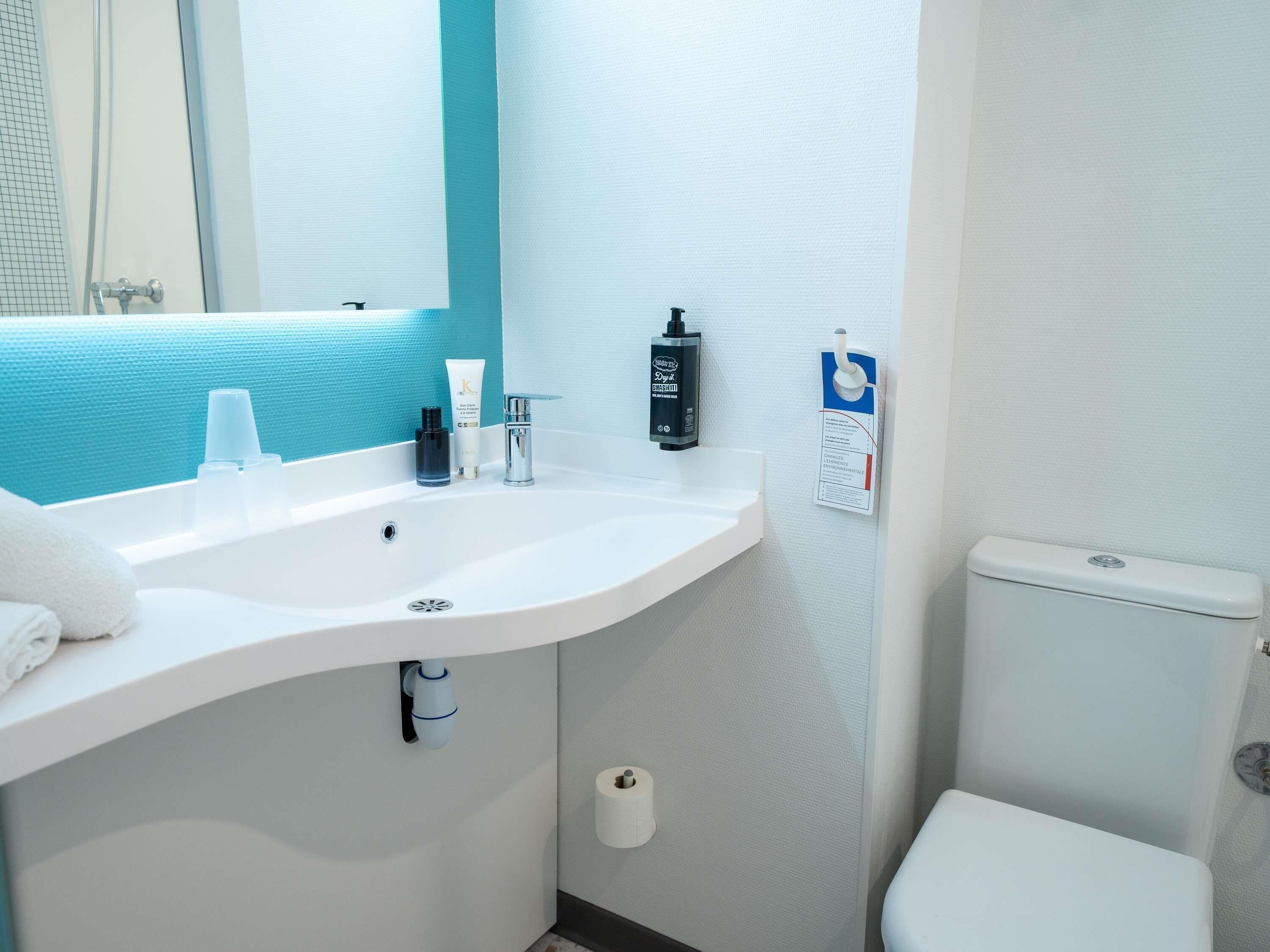 A bathroom with a white sink, a mirror, a toilet, and a blue wall.