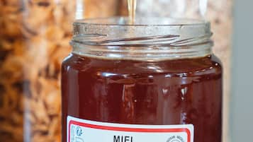Un pot de miel avec un petit ustensile en forme de cuillère pour prélever le miel, dont on fait couler le miel dans le pot.