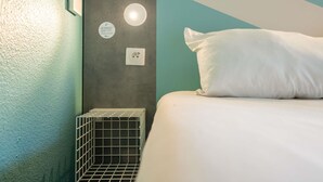 Habitación de hotel ordenada, con cama, una mesita de noche, una lámpara de pared y un enchufe.