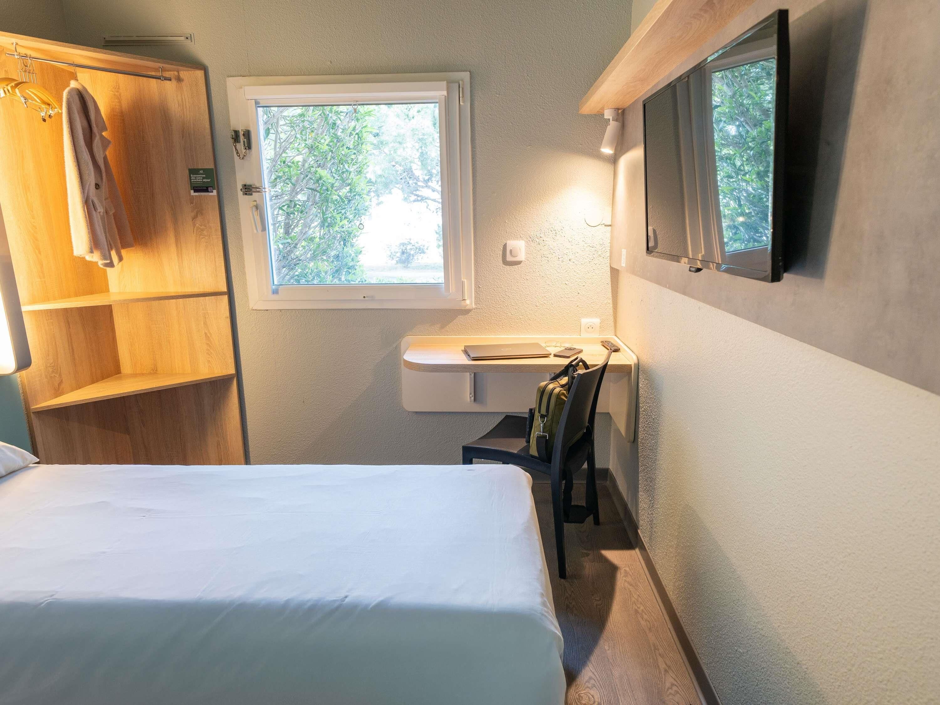 Una habitación pequeña con cama, lavamanos, espejo y ventana.