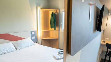 A hotel room with a bed, a desk, a TV, and a wardrobe.