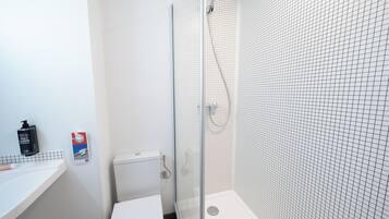A bathroom with a white toilet, a shower with a glass door, and a tiled wall.